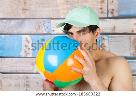 Portrait young handsome man in front of wooden blue vintage background with ball and cap