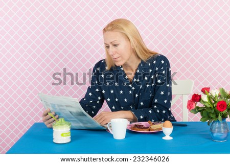 Mature woman reading newspapers in the morning while having breakfast