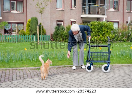 Very old lady with blue walker with red cat by her apartment