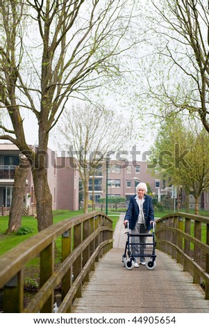 Very old lady with blue walker walking by her apartment