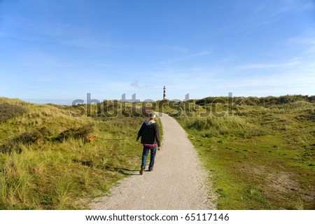 Elderly man is walking with his dog in the dunes with lighthouse