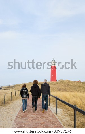 Three persons are walking to the red lighthouse