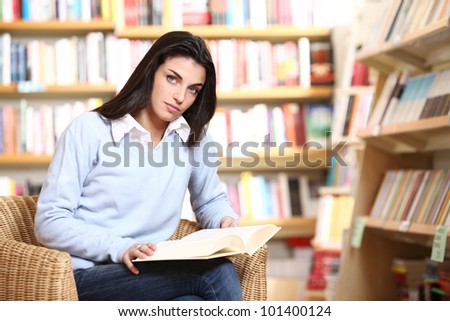 portrait of a seriousfemale student with book in hands looking at camera in a bookstore