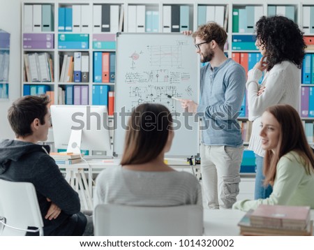 Young researcher giving a lecture to a group of university students, he is writing on a whiteboard and talking