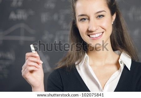 Portrait of a smiling young woman, college student or teacher in front of a blackboard