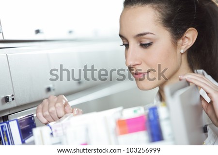 Young female pharmacist reaching for medicine