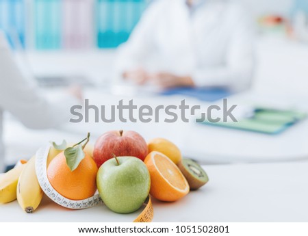 Professional nutritionist meeting a patient in the office and healthy fruits with tape measure on the foreground: healthy eating and diet concept