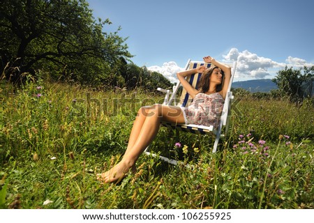 a pretty girl sleeping on a deck chair in the middle of a lawn during a sunny day.