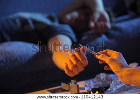 Close up of a young man who gives a joint to his friend lying on the couch