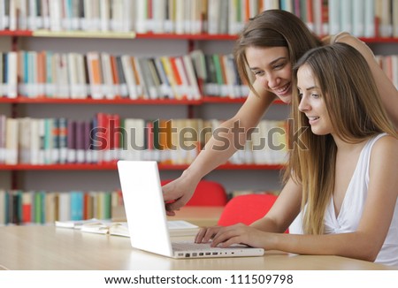 Two young students: young women having fun on laptop at library