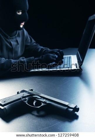 Computer hacker - Male thief stealing data from laptop, focus on gun