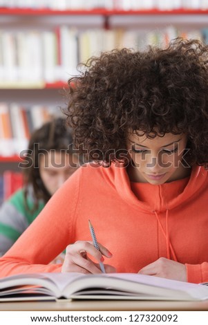 Female student studying in the library, in the background a male student
