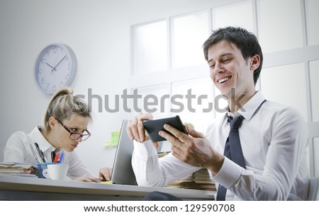 happy businessman using smart phone in office, stressed business woman on background