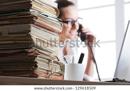 Stack of documents, secretary speaking on the phone in the background