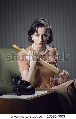 Angry wife waiting for her husband with a rolling pin in hand