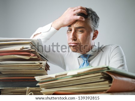 Stressed businessman, with a too much paperwork and files piled up on the table