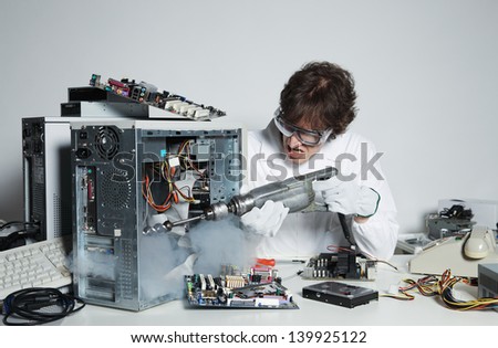 Crazy computer technician is trying to repair a computer with a drill