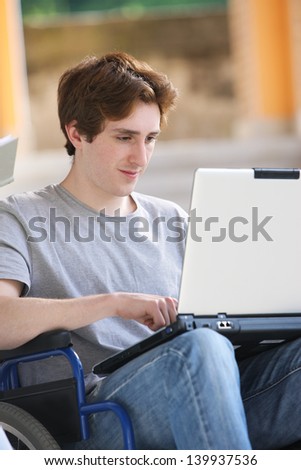 Disabled young man sitting in wheelchair using laptop