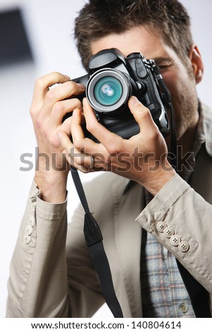 Young man taking photo with professional digital camera, focus on hand and lens