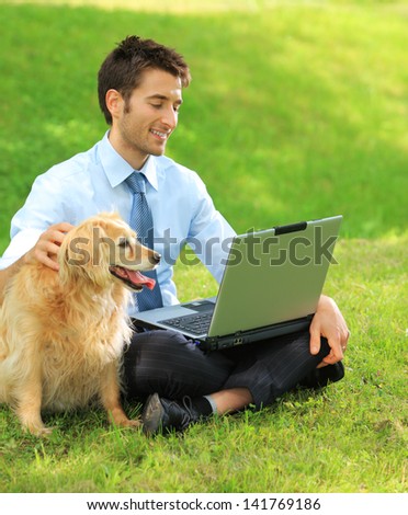 Young business man and his dog working outdoors with laptop on the grass