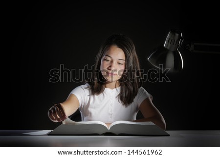 Young girl student, studying late into the night with her book and homework