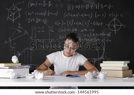 Young student writes in the notebook, in the background a blackboard full of math formulas