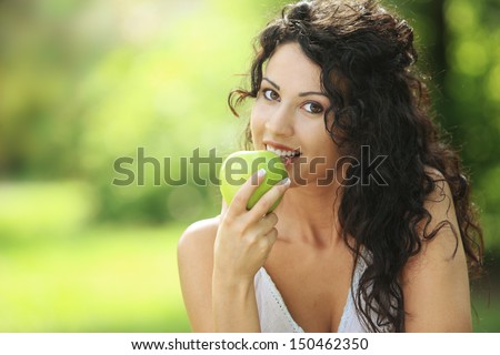 Beautiful cheerful woman eating a green apple, outdoors portrait