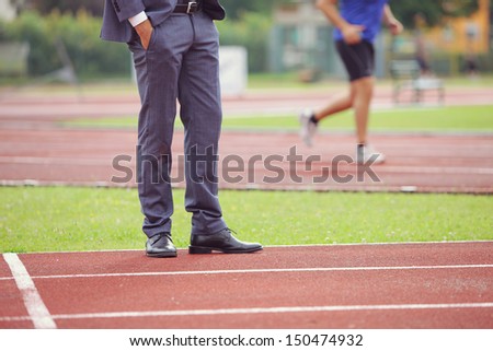Businessman standing on running track, an athlete is running in the background