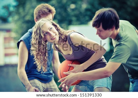 Two boys and a girl playing a game of basketball on an outdoor court.