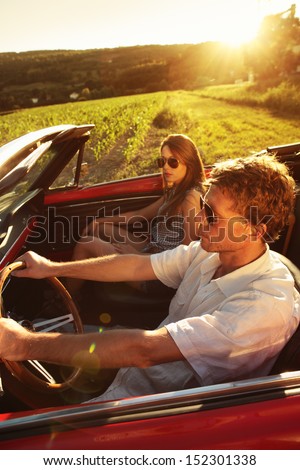 Couple driving vintage convertible car at sunset