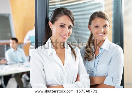 Portrait of two young business woman standing while his team talks in the background