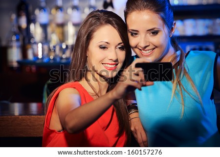 Two happy women at nightclub party taking a self-portrait with smart phone