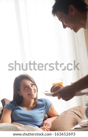 Hand holding breakfast tray to a happy relaxed woman in bed