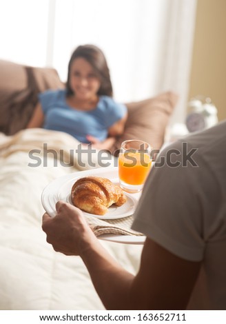 Hand holding breakfast tray to a happy relaxed woman in bed