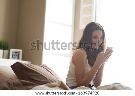 Relaxed woman at home reading a text message in her bright bedroom