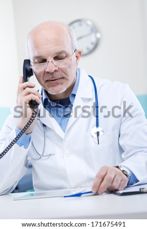 Doctor talking on the phone and holding a thermometer.