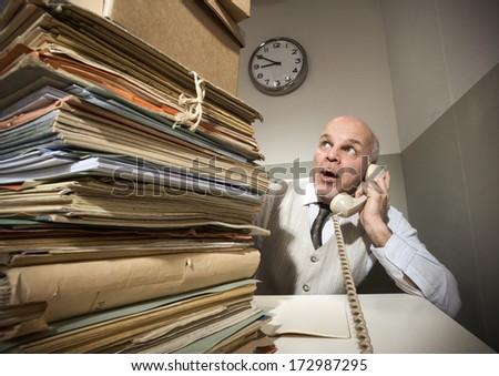 Vintage senior businessman on the phone with a huge stack of files.