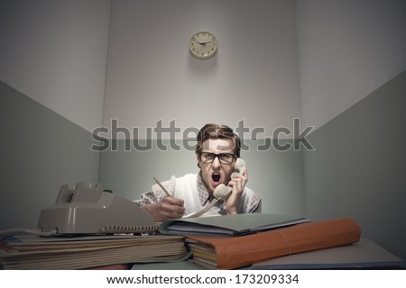Angry nerd guy at the phone with messy desk.