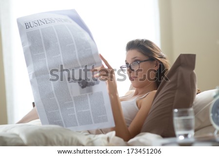 Young woman lying on the bed at home and reading the newspaper