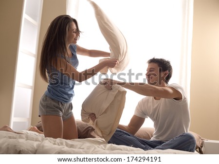 Portrait Of Happy Loving Couple Having A Pillow Fight In Bed