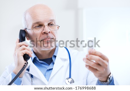 Doctor talking on the phone and looking at medicine\'s bottle.
