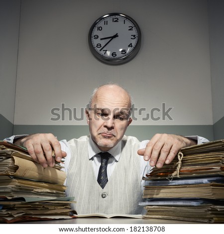 Overworked sad businessman with piles of folders.