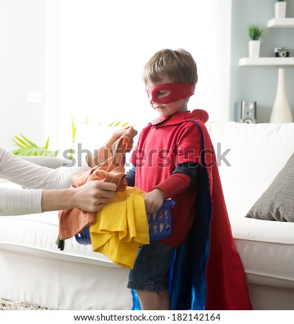 Little superhero boy helping out with laundry and carrying a load of clothing.