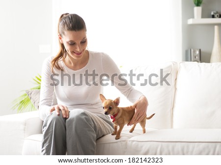 Smiling woman with dog sitting on sofa in the living room.