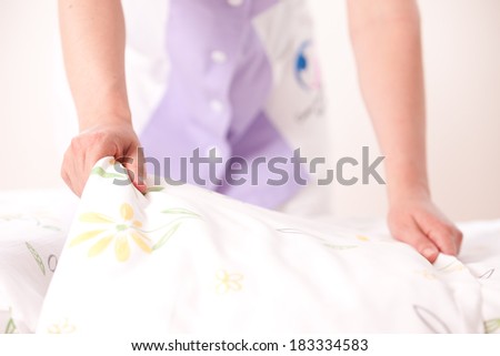 Woman making bed and changing bedding in guest room.