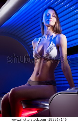 Attractive woman wearing bikini and sitting on tanning bed.