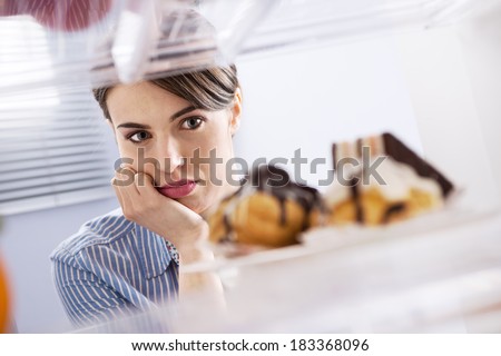 Young hungry woman in front of refrigerator craving chocolate pastries.