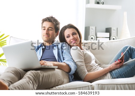 Young couple relaxing on sofa with digital tablet and laptop.