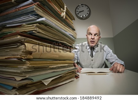 Stressed office worker with a pile of folders in his small room.