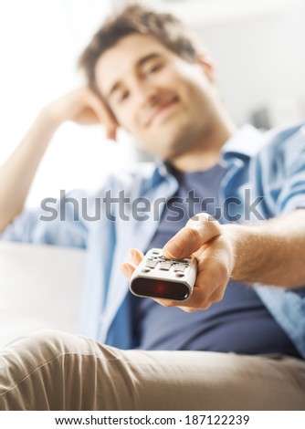Young man relaxing on sofa and holding TV remote control.